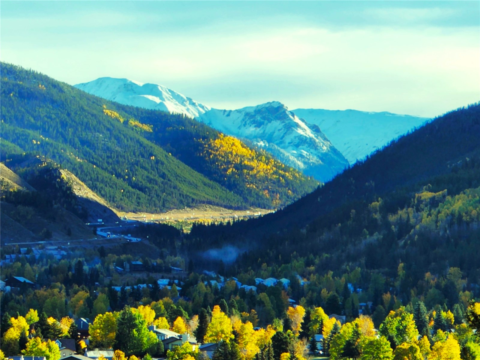 The view from the property: snow-capped peaks of the Tenmile Range rising above a forested valley, with golden aspen on the slopes