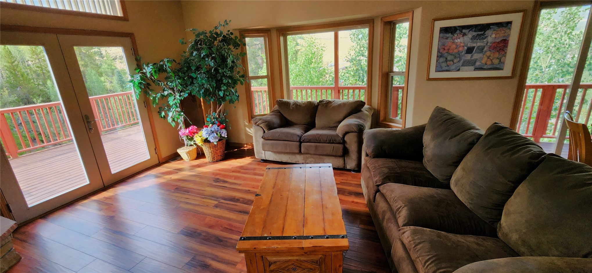 A living area with French doors opening to the wraparound deck, microfiber sofas, hickory floors, and walls of windows on the forest