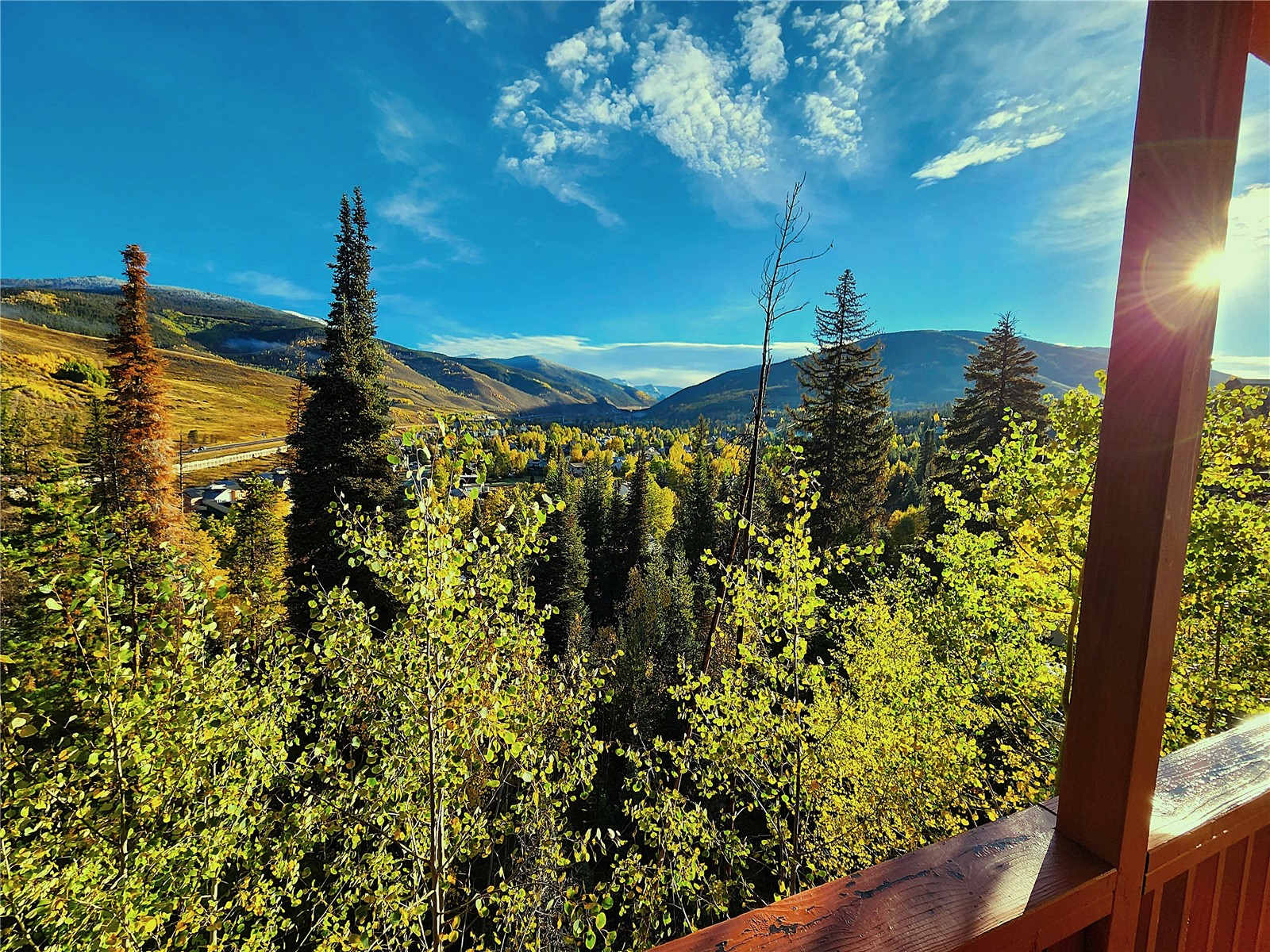 The view from the wraparound deck looking out over aspen and pine to the mountains, with afternoon sun flaring along the deck rail